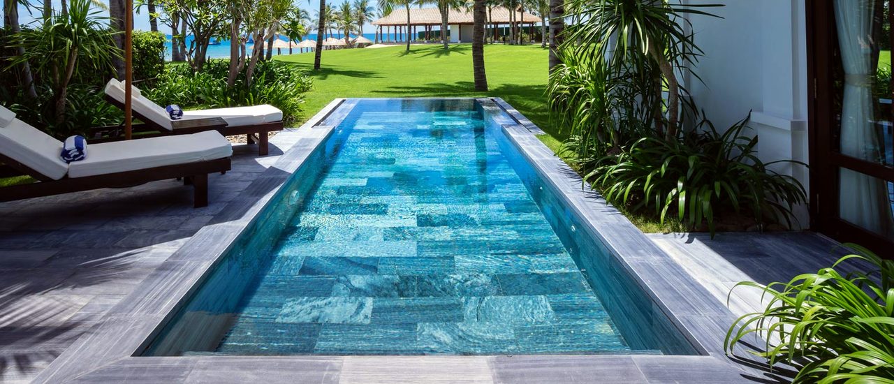A long lap pool on a lawn terrace with loungers under umbrellas